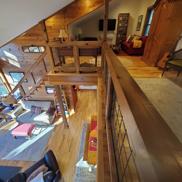A spacious loft-style room with a high ceiling, wooden beams, and a mezzanine level.