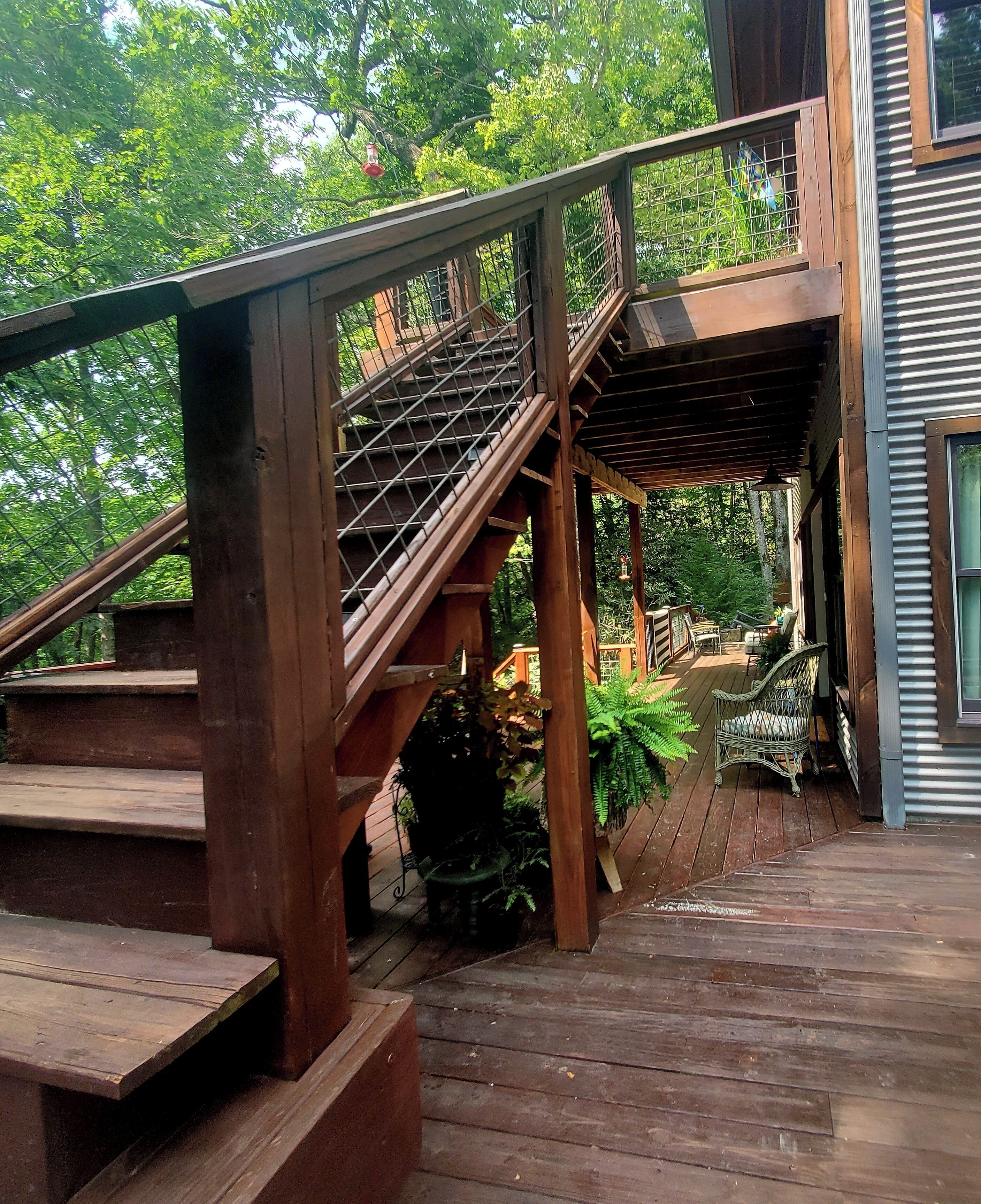 A wooden staircase leading to a covered outdoor area with a view of lush greenery.