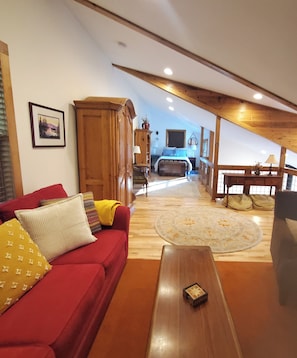 A spacious living area with a red sofa, wooden furniture, and a view of the bedroom in the background.