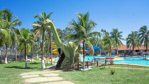 Area piscina con palme, una grande statua a forma di dinosauro e un cielo azzurro limpido.