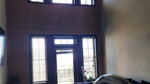A room with a high ceiling, a glass table, a metal chair, and a view of a building through large windows.