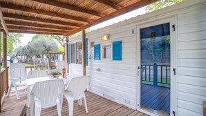 A covered outdoor area with a table and chairs, a wooden deck, and a white building with a blue door.