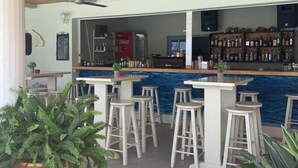 An outdoor bar area with a thatched roof, multiple stools, a bar counter, and a variety of bottles.