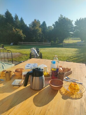 Desayuno dispuesto en una mesa al aire libre, con vistas a un campo de césped y árboles.