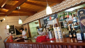 Una zona de bar con techo de madera, lámparas colgantes y una barra con botellas y vasos.