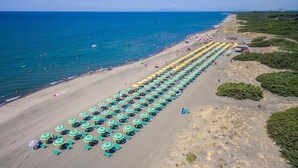 An aerial view of a beach with rows of umbrellas and sun loungers, a clear sky, and the ocean in the background. - Vacation Village California Superior Vulci Cottage for 4 persons (Montalto Marina)