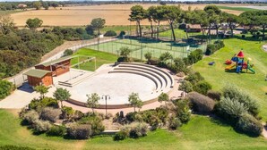 An outdoor amphitheater with tiered seating, surrounded by greenery and a playground. - Vacation Village California Superior Vulci Cottage for 4 persons (Montalto Marina)