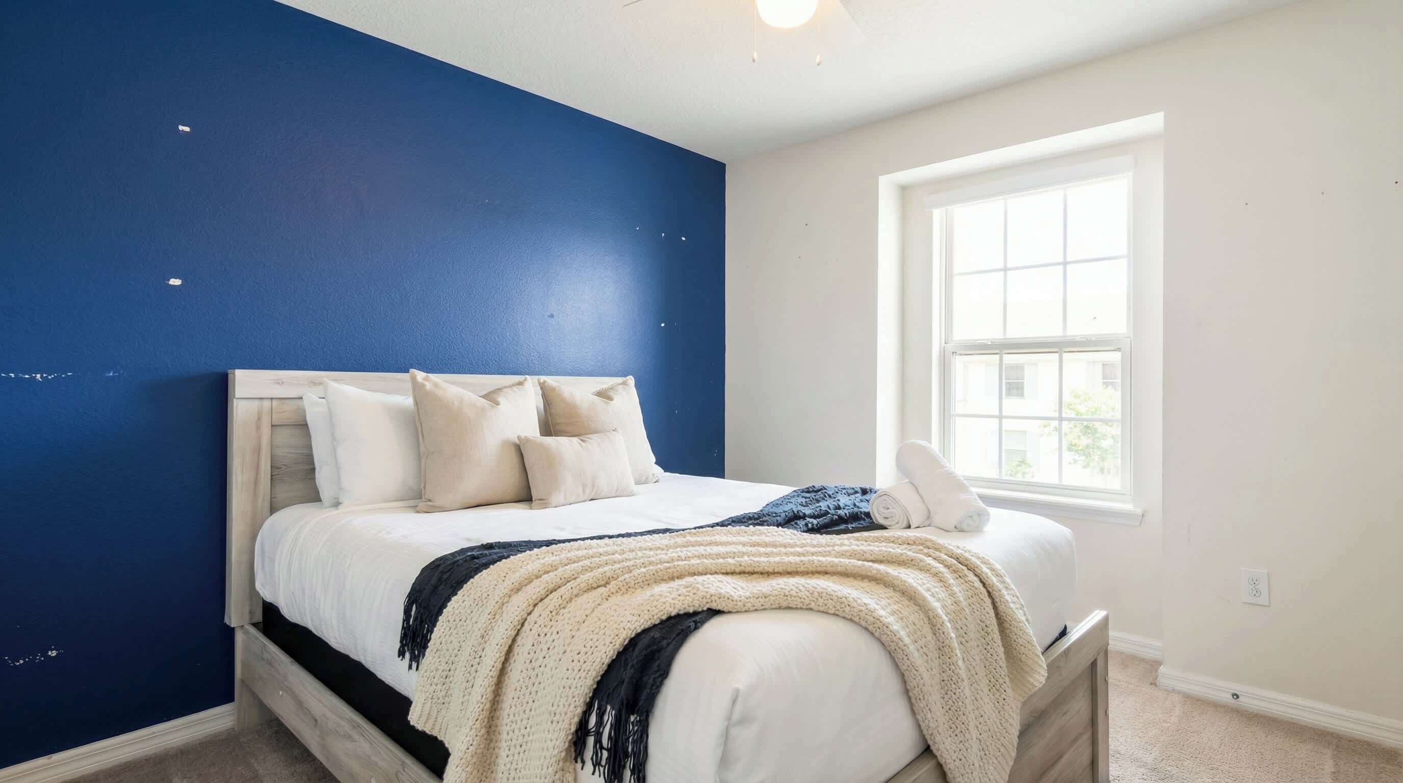 A bedroom with a bed, pillows, a window, and a blue wall.