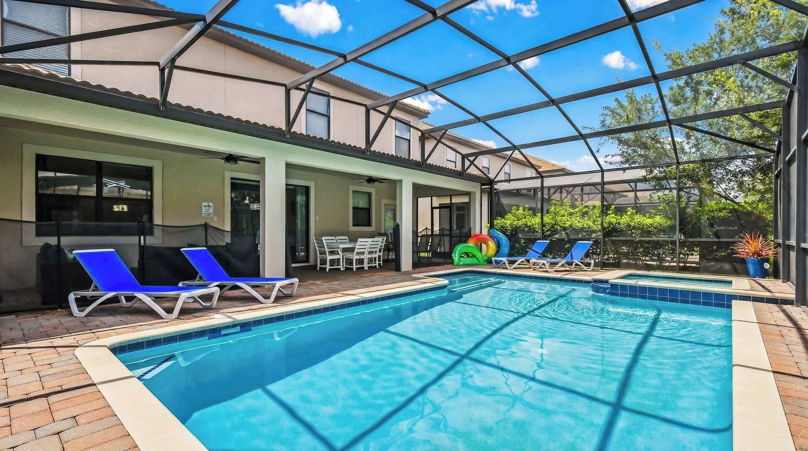 An indoor swimming pool with lounge chairs, a table, and a covered patio area.