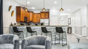 Une cuisine moderne avec des meubles en bois, un plan de travail en granit et un coin bar doté de chaises noires.