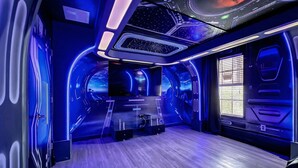 Ein futuristisches Zimmer mit gewölbter Decke, einem großen Bildschirm und einem Fenster mit Jalousien.