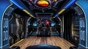 A futuristic room with a central seating area, a large screen displaying a space scene, and a circular window with a planet view. - Huge Home With Game Room & Theater Near Disney 1429 (Davenport)