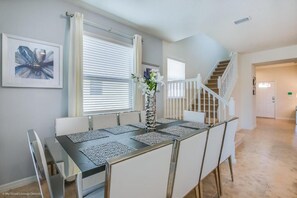 Een eetgedeelte met een tafel voor vier personen, witte stoelen, een vaas met bloemen en een trap naar een ander niveau.