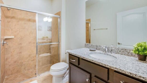 Een moderne badkamer met een douchecabine van glas, een wit toilet, een wastafel met granieten blad en een grote spiegel.