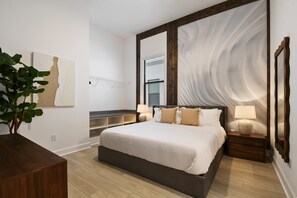A modern bedroom with a large bed, bedside tables, a mirror, and a wall art piece.