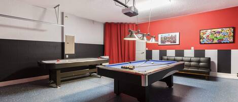 A pool table with a billiards cue, a red curtain, a black and white striped wall, and a black leather couch.