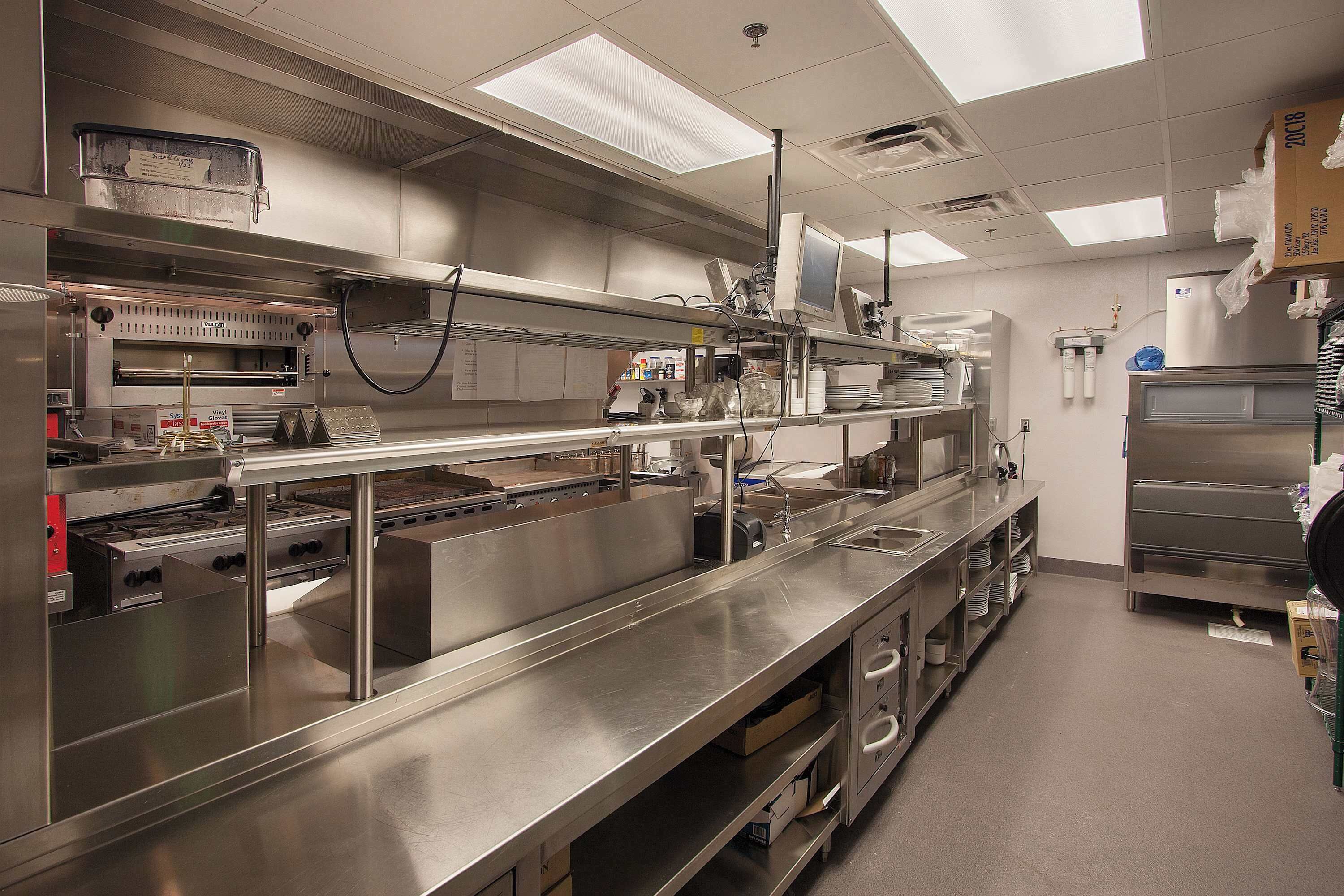 Une cuisine professionnelle équipée d’appareils en acier inoxydable, d’un long comptoir et d’un éclairage suspendu.