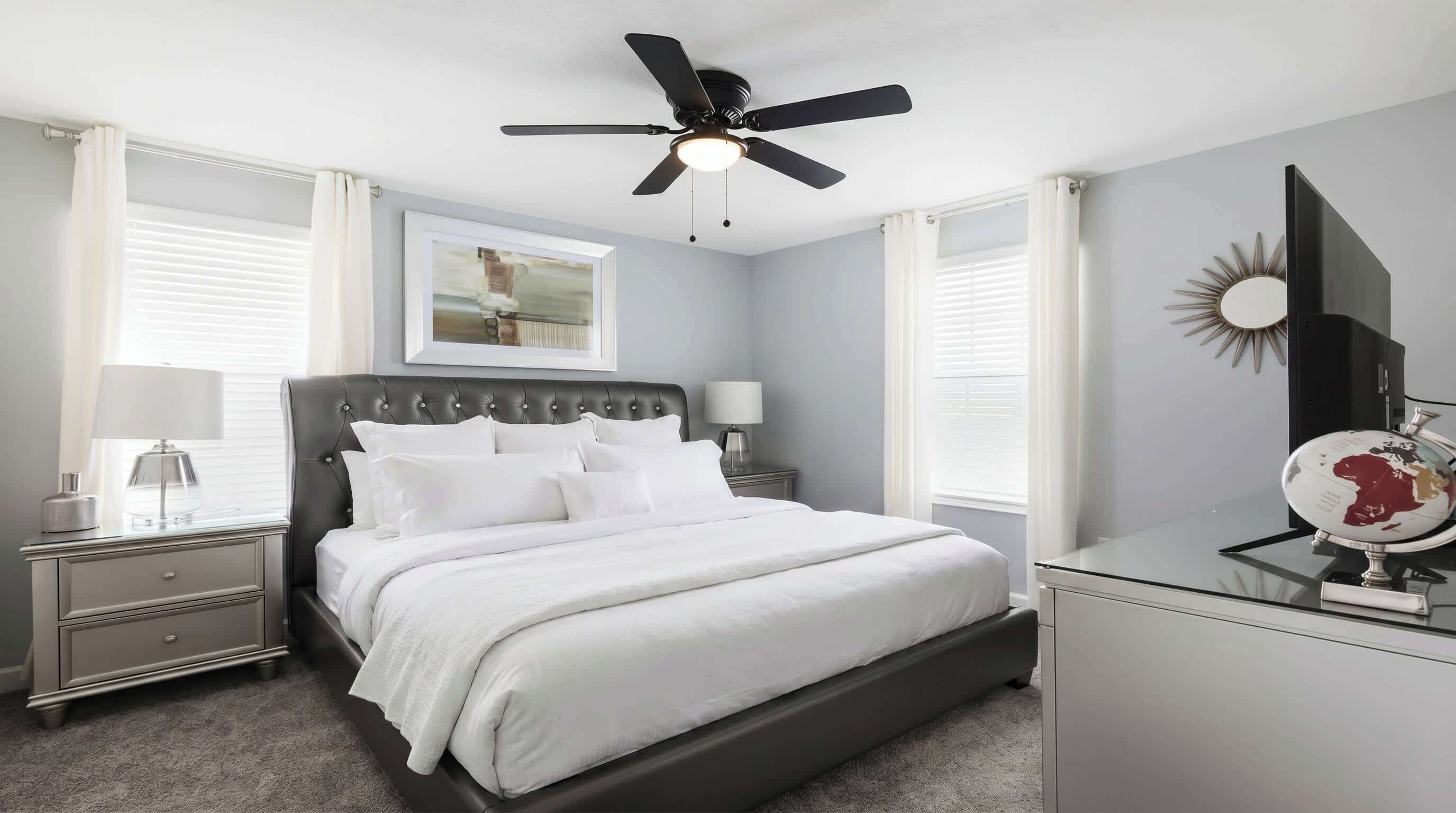 A bedroom with a bed, nightstands, a ceiling fan, a framed picture, a globe, and a dresser.