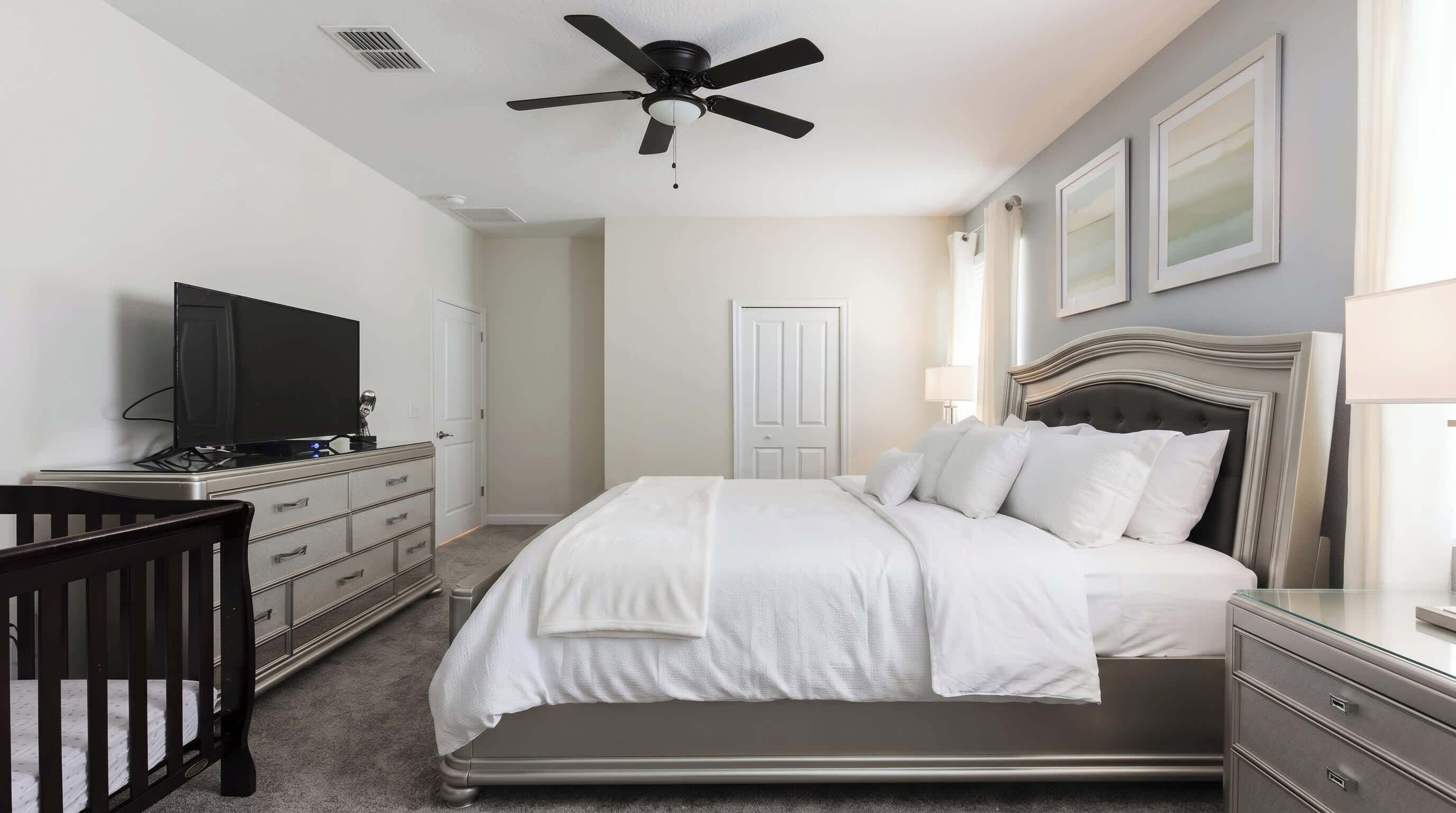 Une chambre à coucher comprenant un lit, un téléviseur, un ventilateur de plafond, une commode et une porte.
