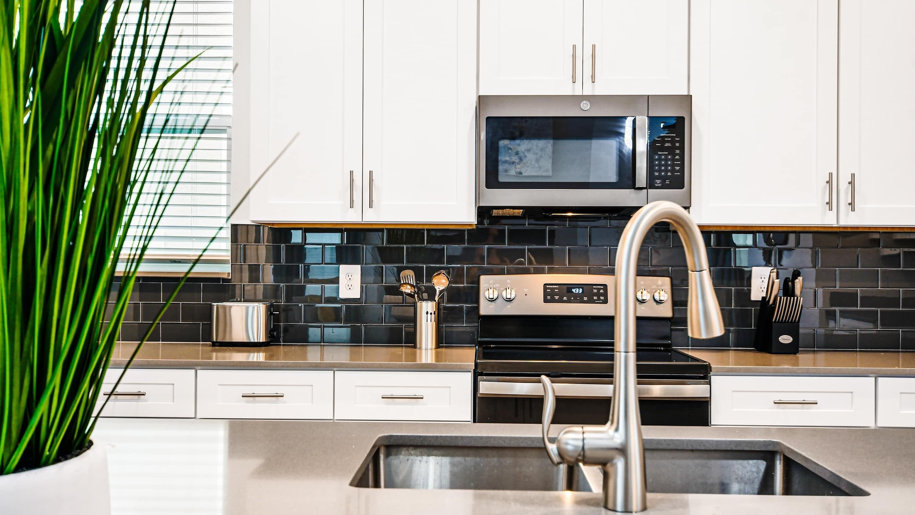 A modern kitchen with white cabinets, a stainless steel microwave, a built-in oven, and a sink with a modern faucet.