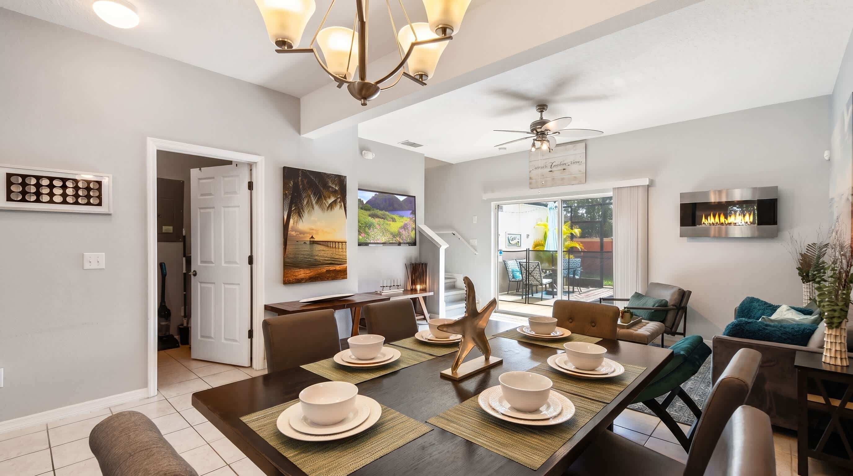 A modern dining area with a large table set for six, a ceiling fan, and a fireplace.