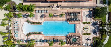 An aerial view of a resort with a central swimming pool, sun loungers, and palm trees.