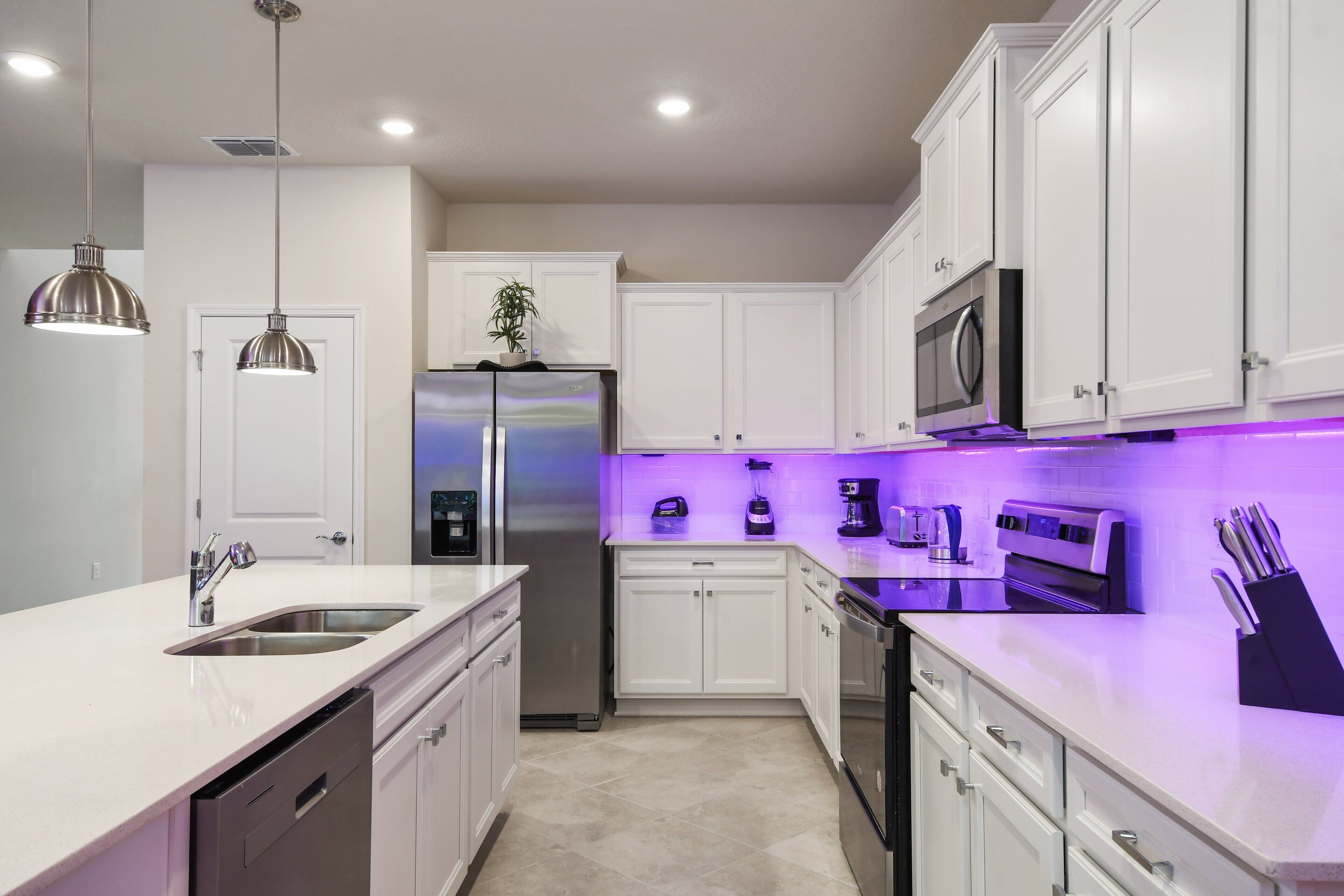A modern kitchen with white cabinetry, stainless steel appliances, and pendant lighting.