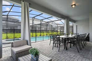 A covered patio with a pool, outdoor seating, and a table with chairs.