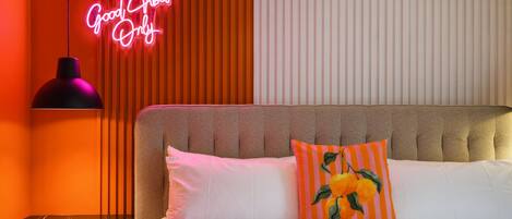 Ein Schlafzimmer mit einer Neonreklame, gestreiften Kissen und einem gepolsterten Kopfteil.