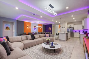 A modern living room with a sectional sofa, a coffee table, and a kitchen area with white cabinets and a bar.