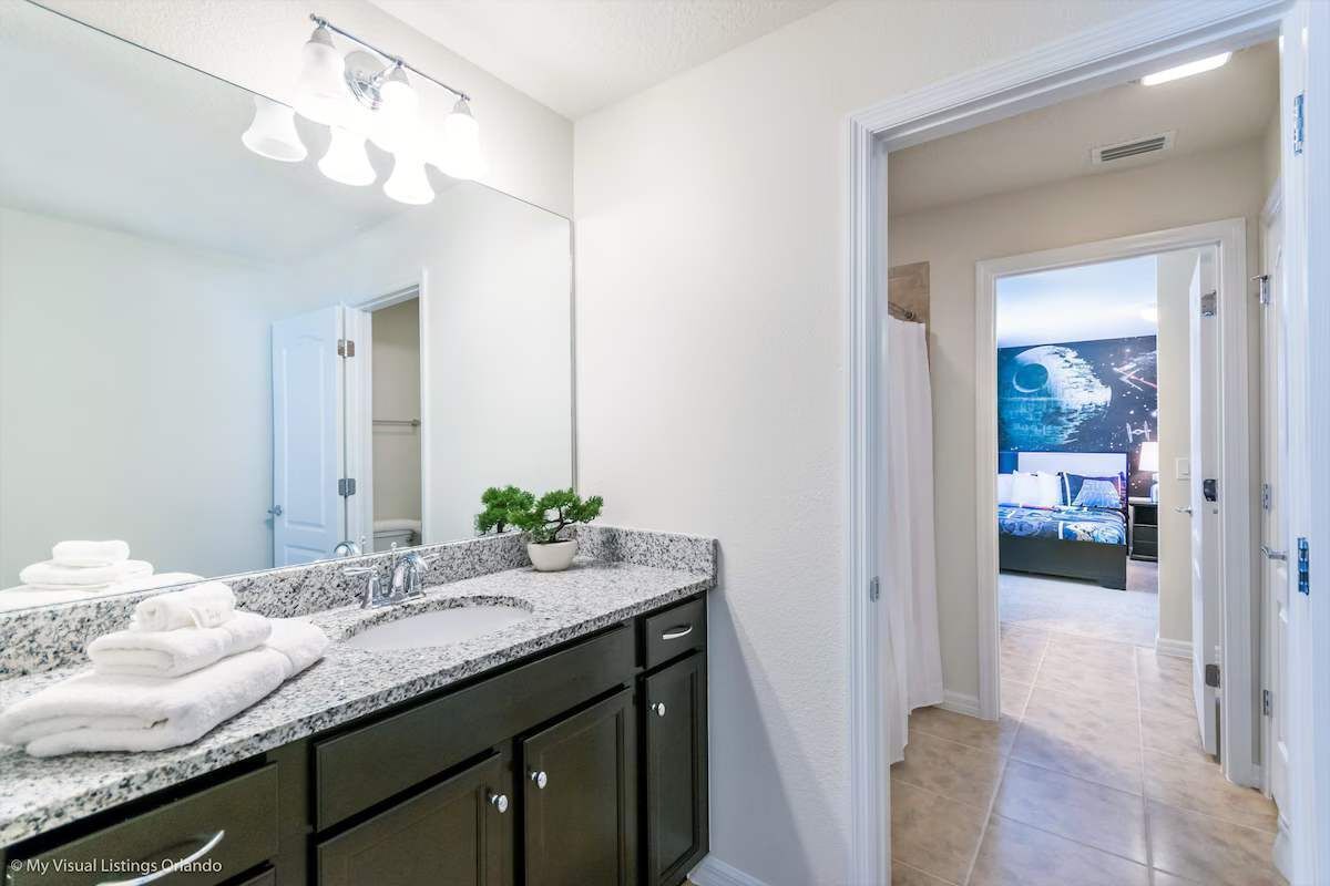A modern bathroom with a granite countertop, dark cabinets, and a large mirror. There is a small potted plant on the countertop.