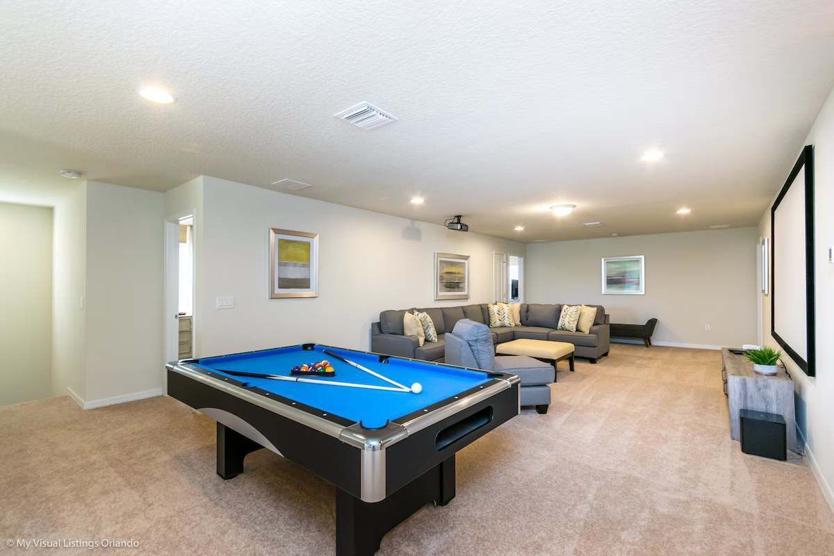 A pool table in a living room with a sofa and a projector screen.
