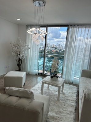 Un salon moderne avec une grande fenêtre, un canapé blanc, un tapis moelleux et une plante décorative.