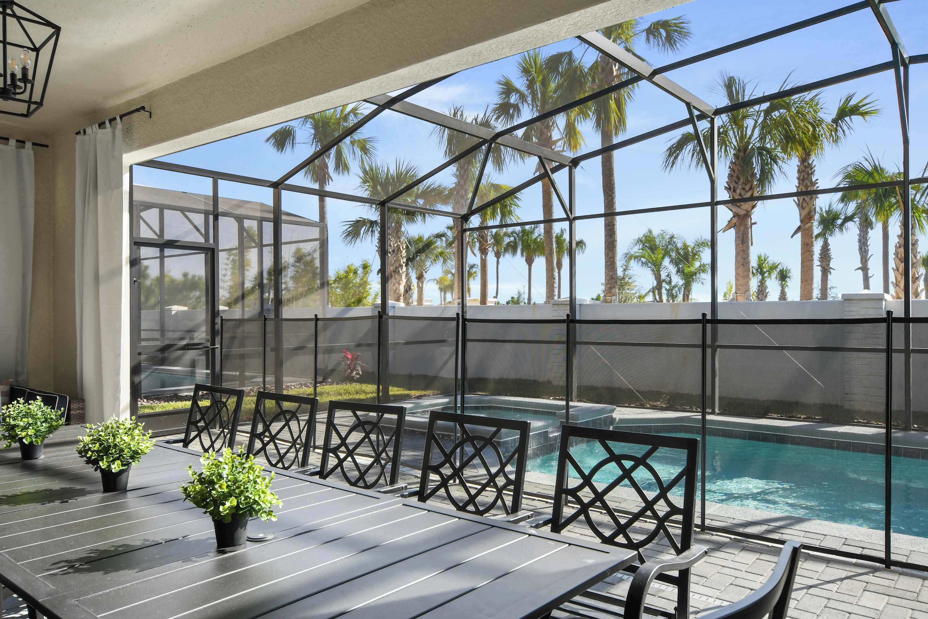 Un espace aménagé au bord de la piscine, doté d’une structure en verre, de sièges extérieurs et offrant une vue sur les palmiers.