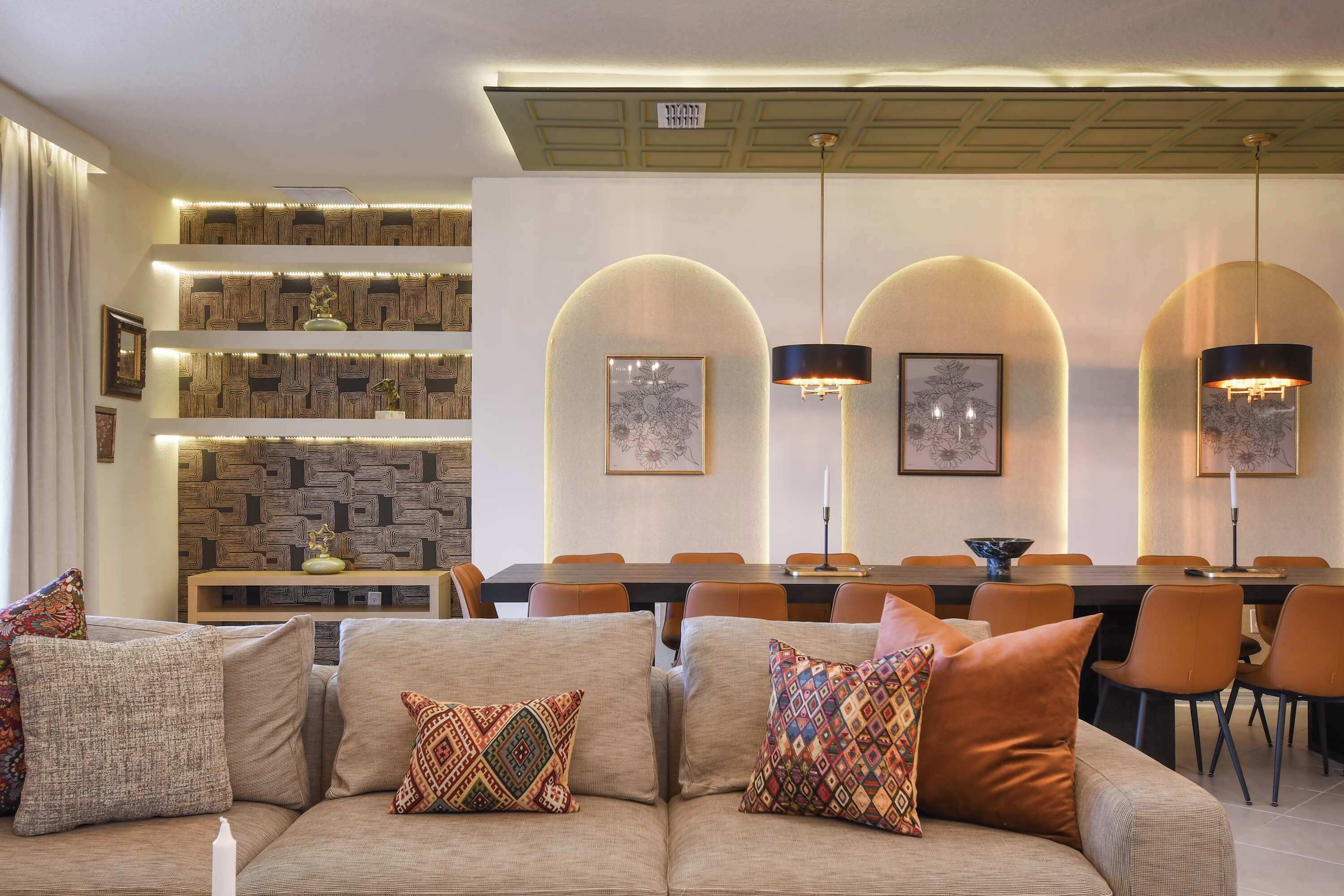 Een moderne woonkamer met een bank, gestreepte kussens, een eethoek met een tafel en stoelen, en decoratieve wandplanken.