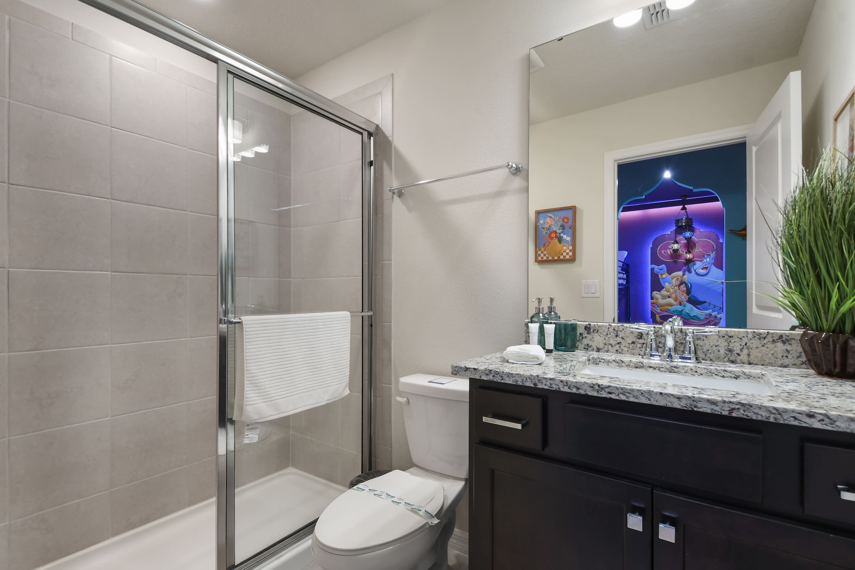 A modern bathroom with a glass shower enclosure, a toilet, and a sink with a granite countertop.