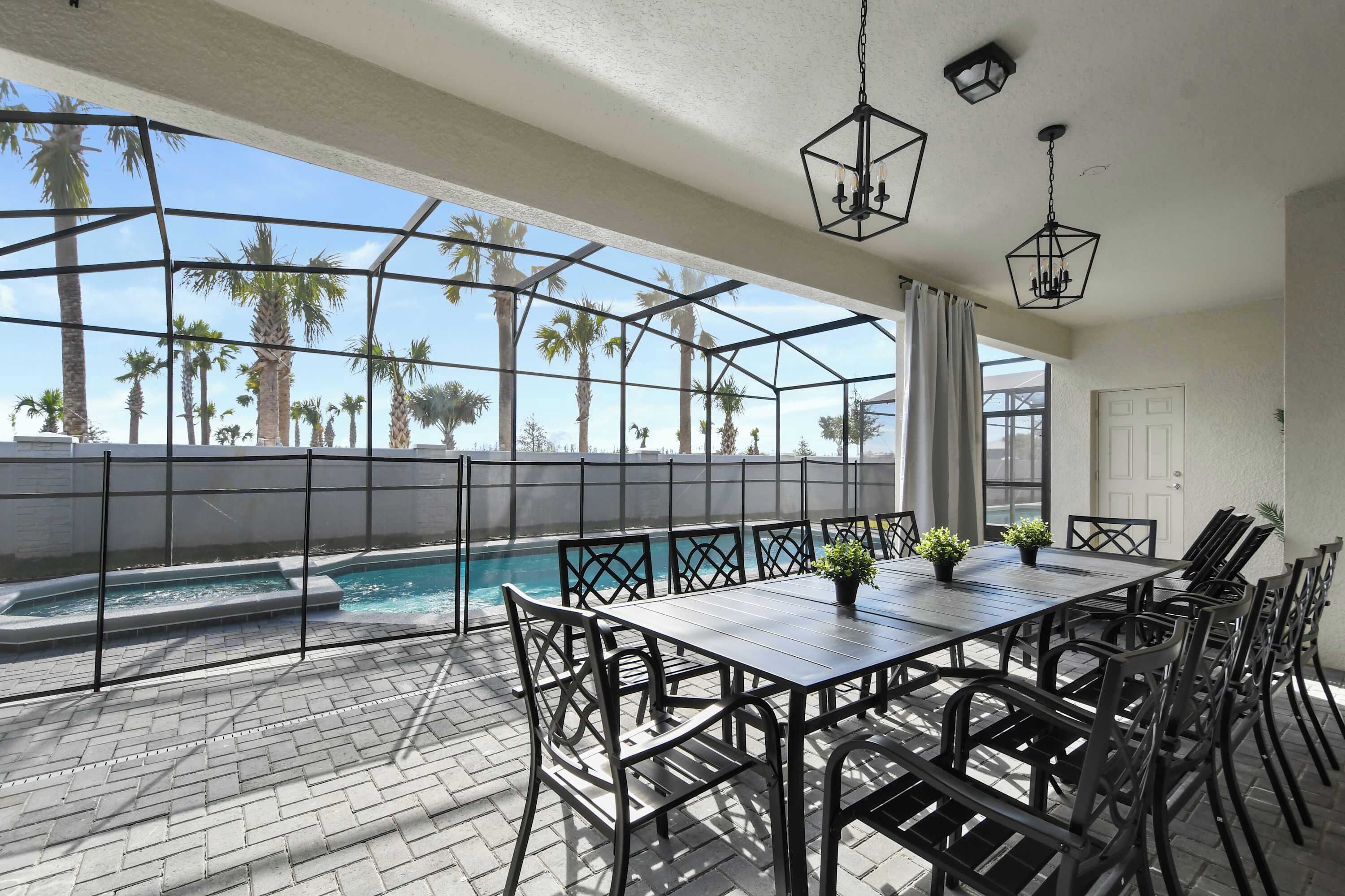 A covered outdoor patio with a pool, a dining table with chairs, and hanging lights.