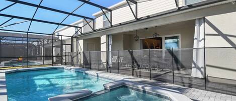 An indoor swimming pool with a glass ceiling, surrounded by a white building with a patio area.