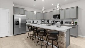 Een moderne keuken met een centraal eiland, roestvrijstalen apparatuur en hanglampen.