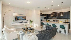 A modern living room with a sofa, chairs, a coffee table, and a TV mounted on the wall. - Elegant 5-bedroom Villa w Private Pool Near Disney (Davenport)