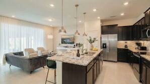 A modern kitchen with dark cabinets, a stainless steel refrigerator, and a marble island. - Elegant 5-bedroom Villa w Private Pool Near Disney (Davenport)