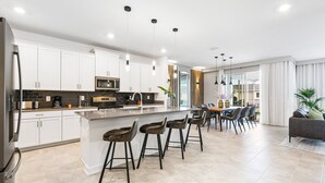 Une cuisine moderne avec des meubles blancs, un îlot central doté de tabourets, des appareils en acier inoxydable et un éclairage suspendu.