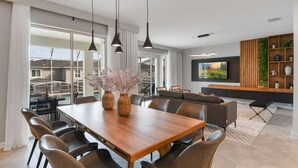 Un salon moderne avec une table à manger en bois, des fauteuils en cuir et un grand téléviseur fixé au mur.