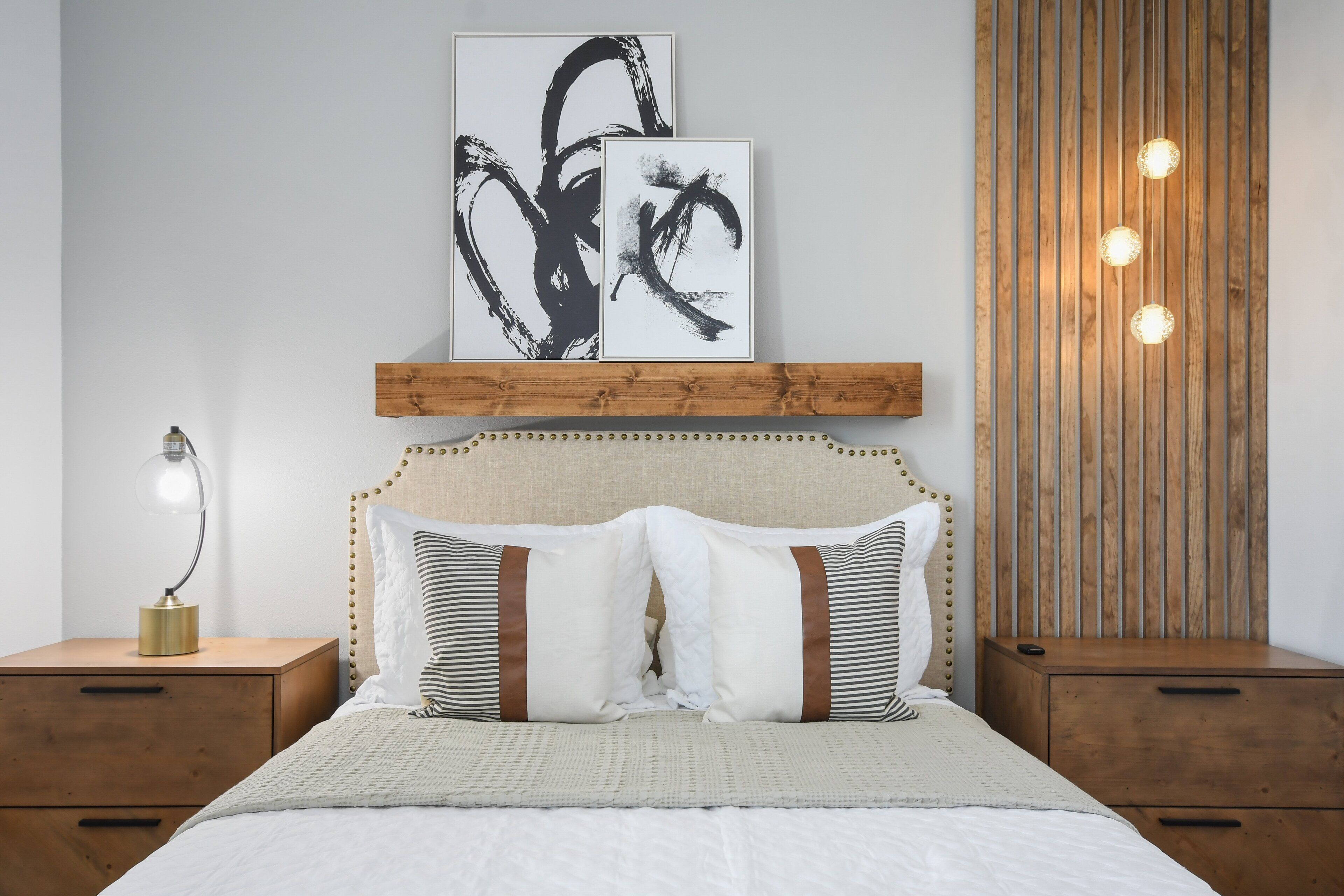 Un dormitorio ordenado con cama, mesitas de noche y obras de arte.