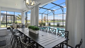 Ein großzügiger Patio-Bereich mit langem Tisch und Stühlen, einem Blumentopf und Blick auf Pool und Gartenlandschaft.