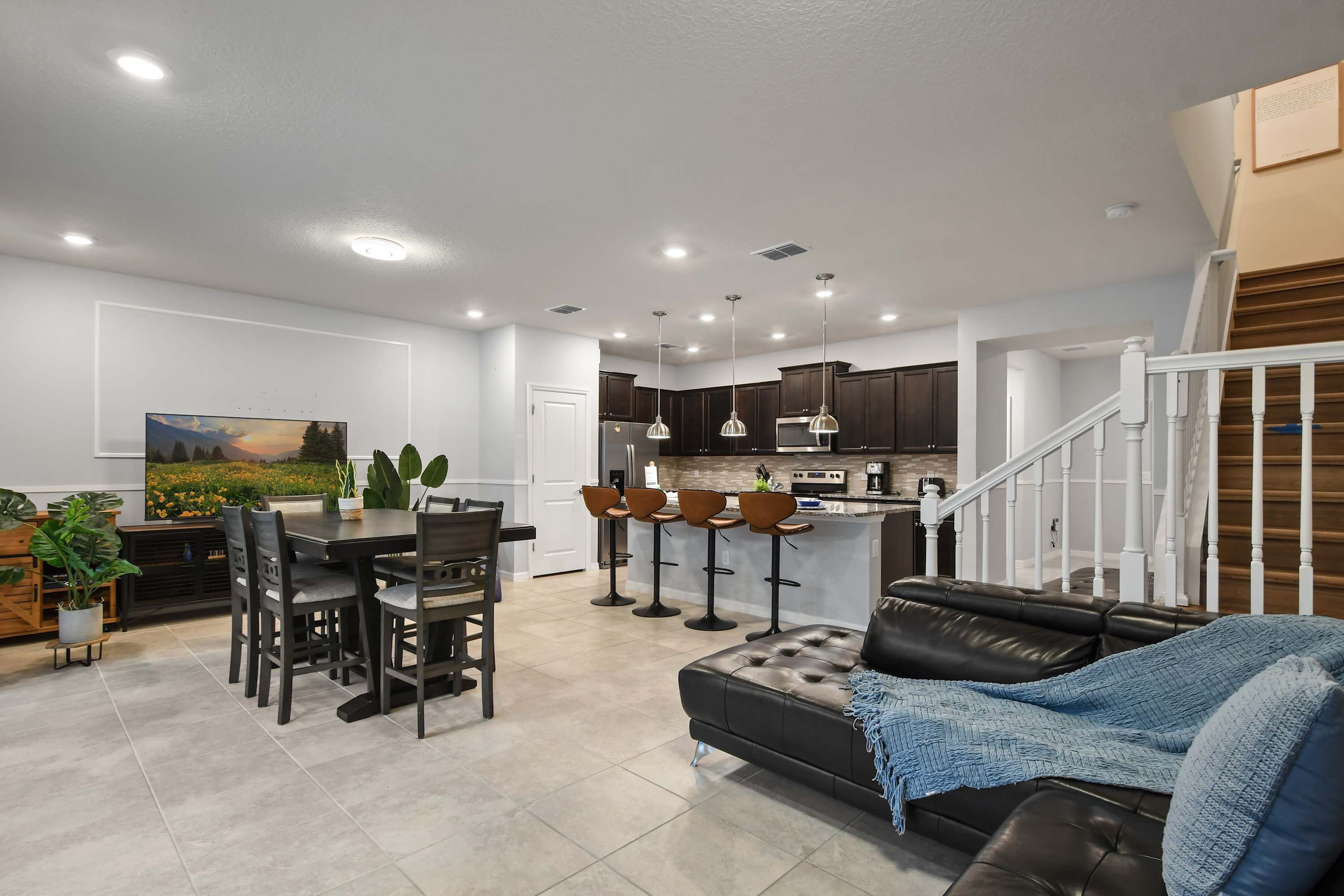 A modern kitchen with dark cabinets, a dining area with a table and chairs, and a staircase leading to an upper level.