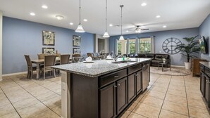 A modern kitchen with a central island, dark cabinetry, and a dining area with chairs and a table. - Ultimate 8BR Family Fun in Resort Near Disney! (Kissimmee)