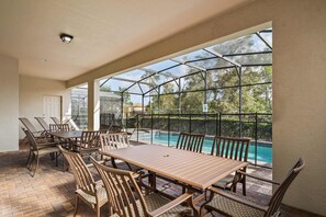 A covered patio area with a pool, featuring a table and chairs, and a view of the pool through a glass enclosure. - Ultimate 8BR Family Fun in Resort Near Disney! (Kissimmee)
