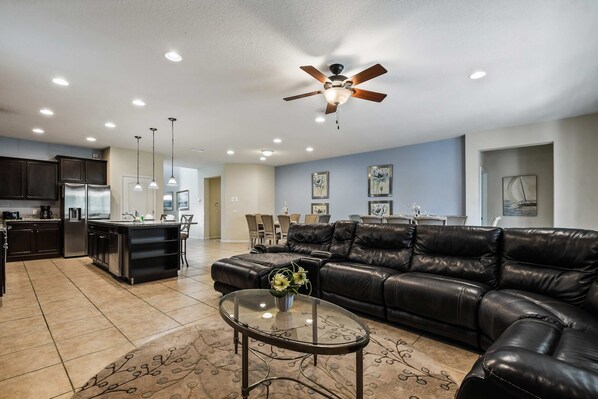 A modern living room with a leather sofa, a glass coffee table, and a ceiling fan.