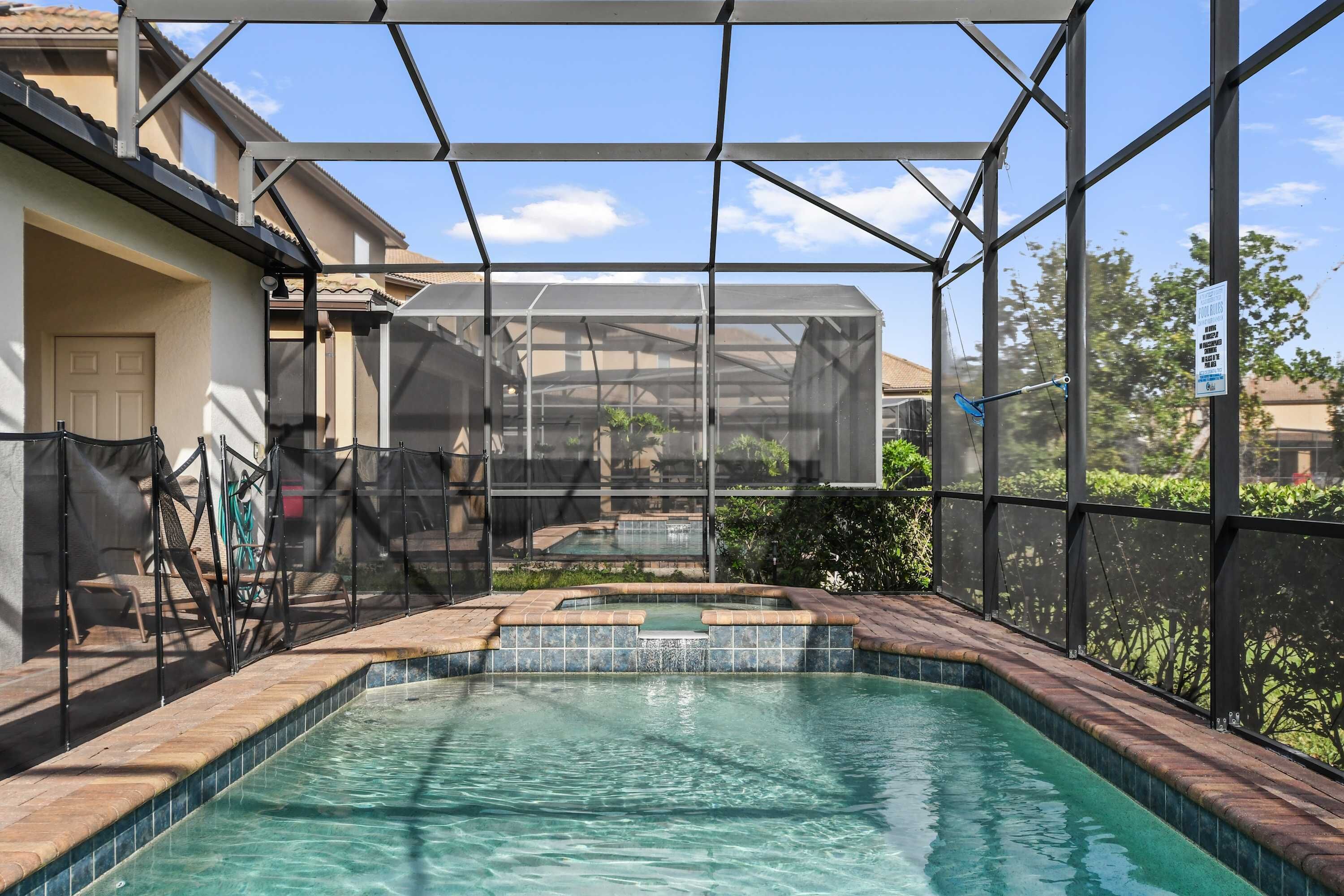 A swimming pool with a glass enclosure, surrounded by a patio area with chairs and a hose.